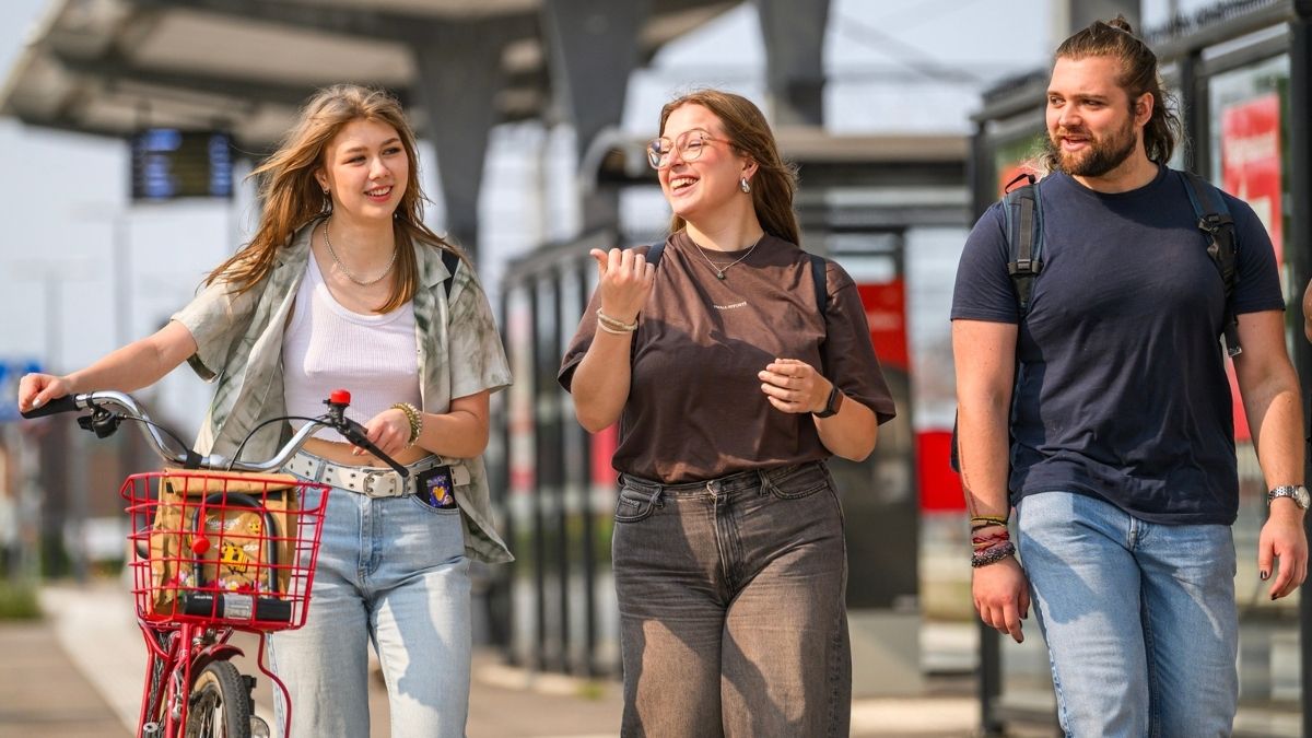 Tre unga personer promenerar och cyklar tillsammans vid en station i Blekinge – symbol för regionens livskvalitet, gemenskap och hållbara livsstil.