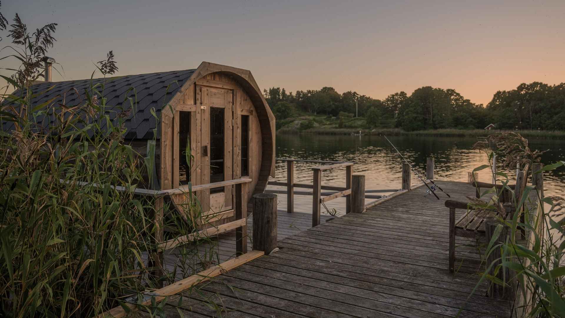 Vedeldad bastu vid brygga i Blekinge med stilla sjö, vass och kvällsljus.