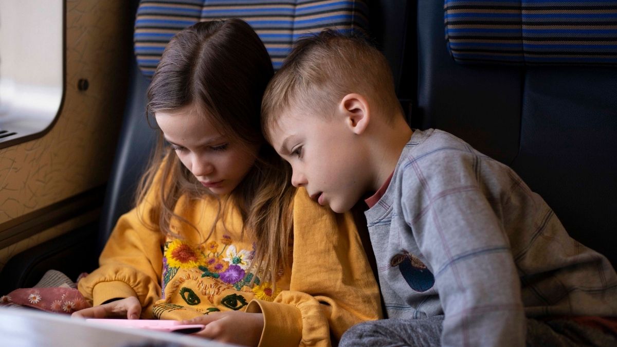 Två barn som sitter tillsammans på tåget och tittar på en skärm – lugn och trygg resa med kollektivtrafik i Blekinge.