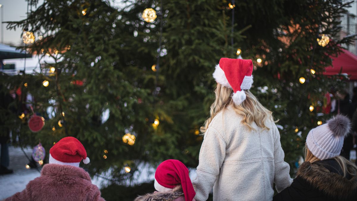 Familj i tomteluvor beundrar julgran med lysande ljus i Blekinge under vinterkväll