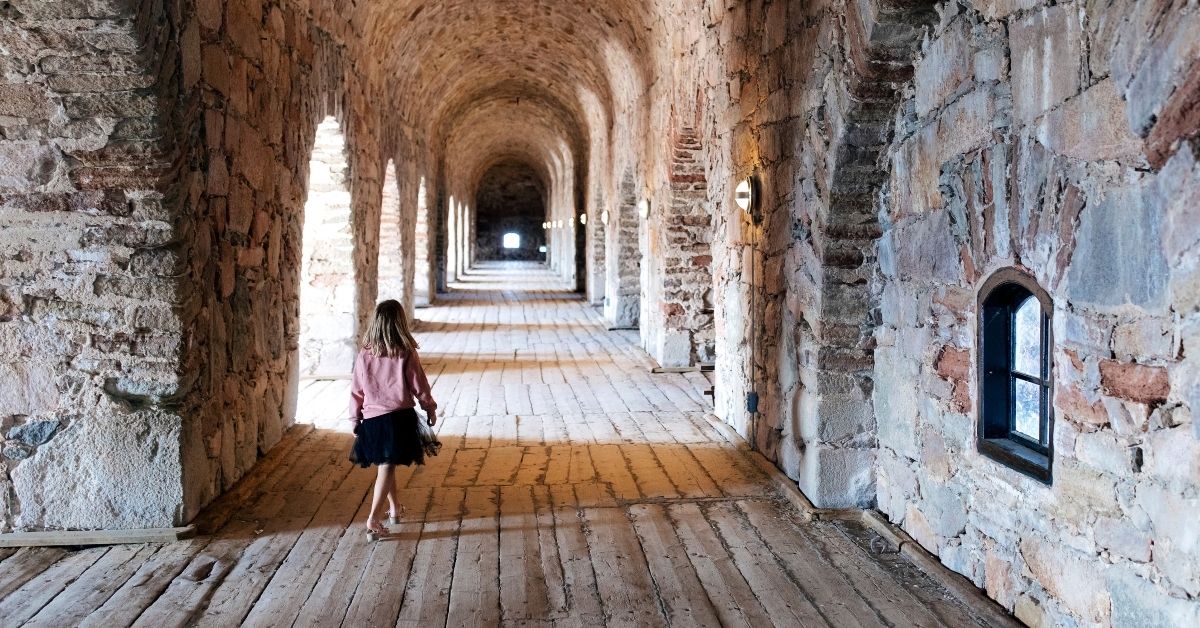 Barn som utforskar historiska stenvalv i en borgmiljö med lång korridor och medeltida arkitektur på Drottningskärs kastell i Blekinge.