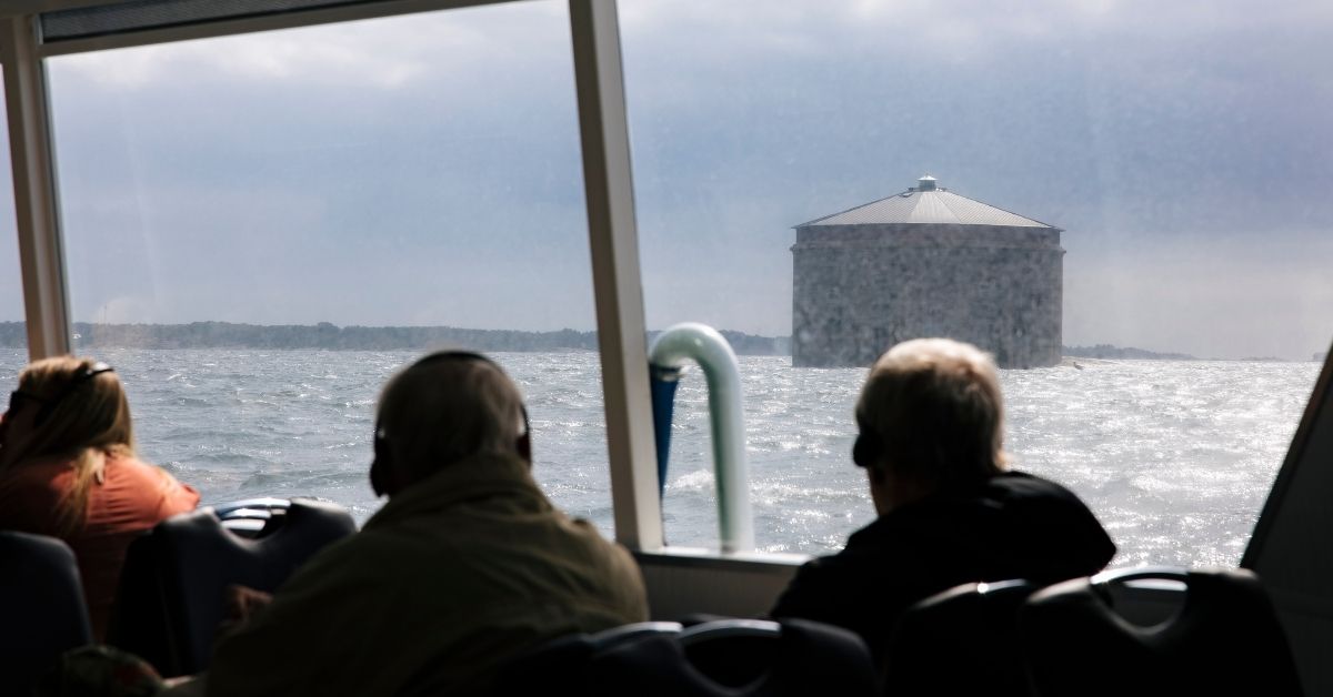 Utsikt från båtresa i Blekinge skärgård mot Kungsholms fort utanför Karlskrona, med resenärer som njuter av havsvyn.