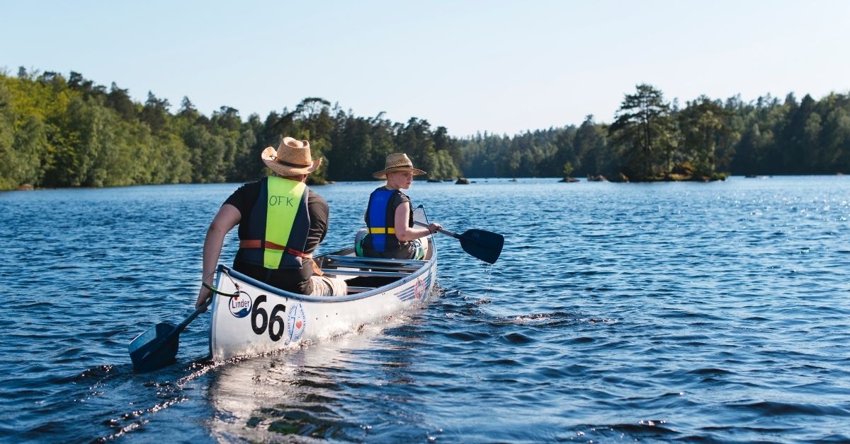 Två personer paddlar kanot på sjön Halen i Olofström, omgivna av skog och klart vatten under en solig sommardag.