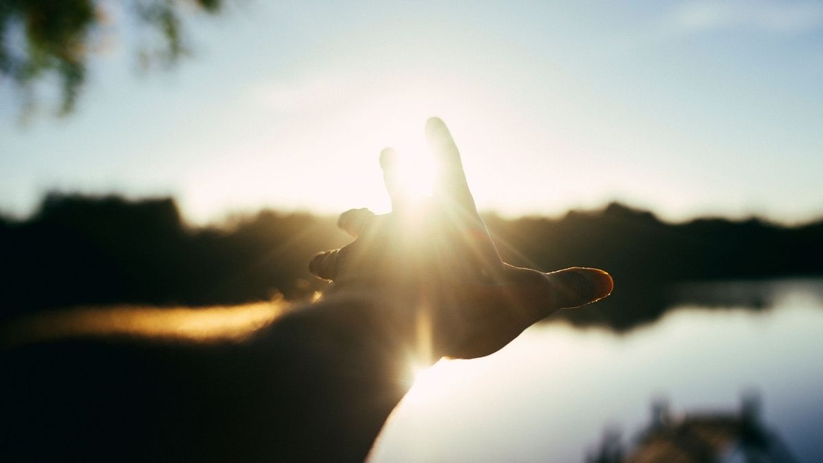 Hand sträcker sig mot soluppgång över sjö i Olofström, Blekinge