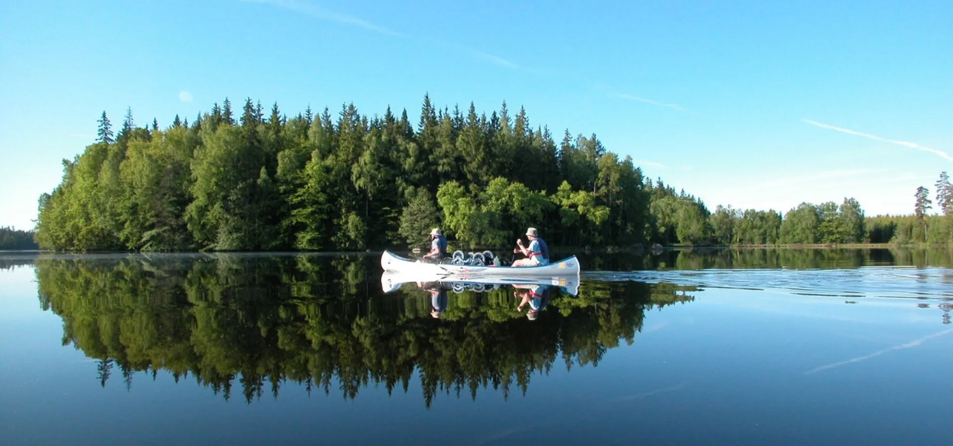 Sjön Halen i Blekinge, stilla vatten, en kanot med två kanotister förbi en lite skogsbeklädd ö