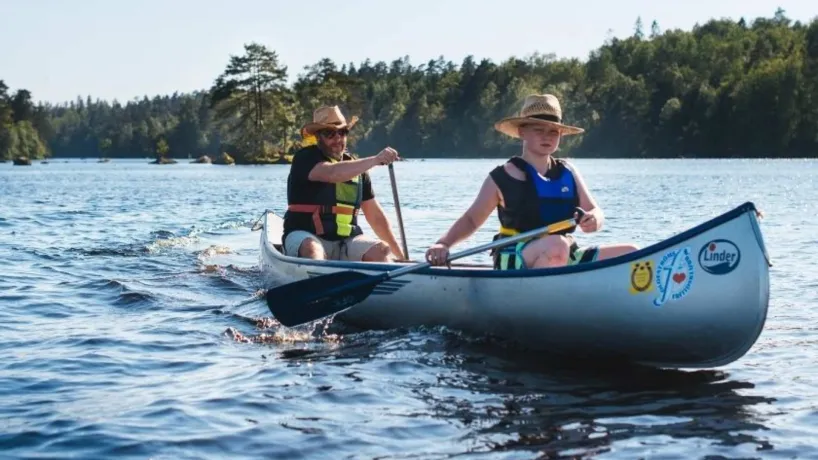 Två personer paddlar kanot över spegelblank sjö omgivna av skog i Blekinges inland.
